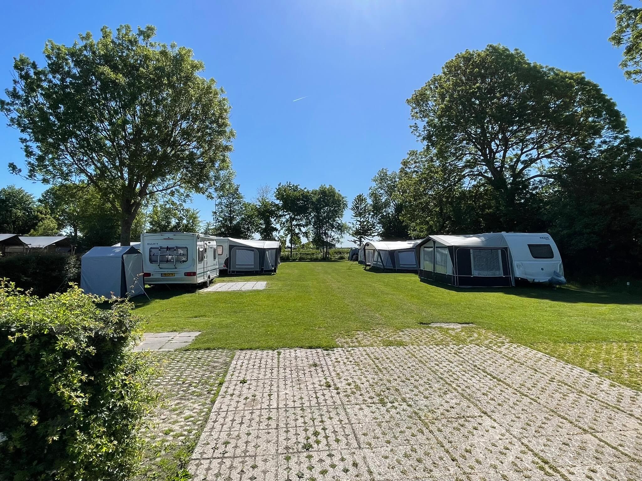 Campingplaatsen met caravans en luifels op een grasterrain op een zonnige dag - klantreis campingwebsite